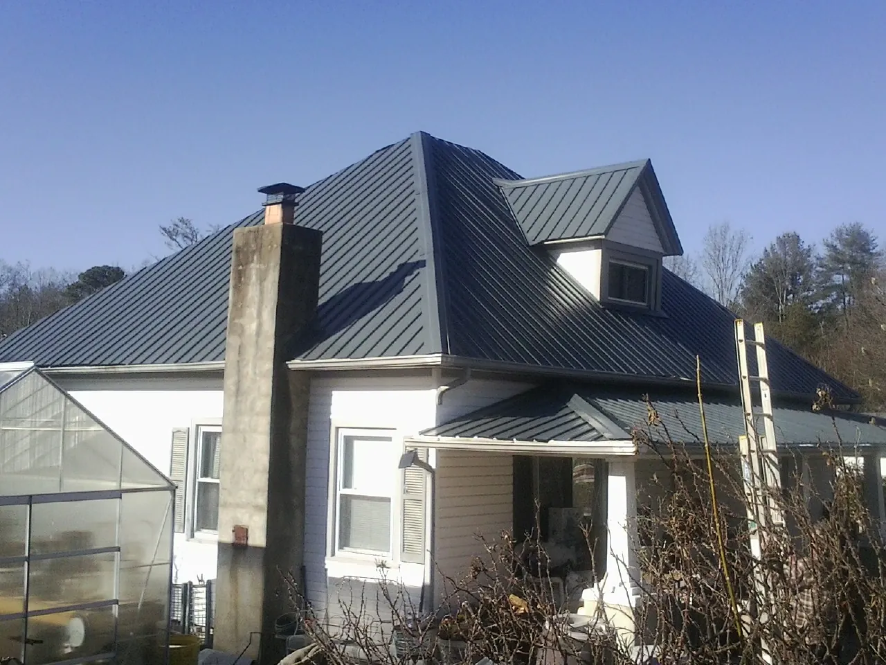 Dark blue standing seam metal roof on a white farmhouse with dormer — Slate & Tile Roof Repair by Roofing Brothers in Ihlen