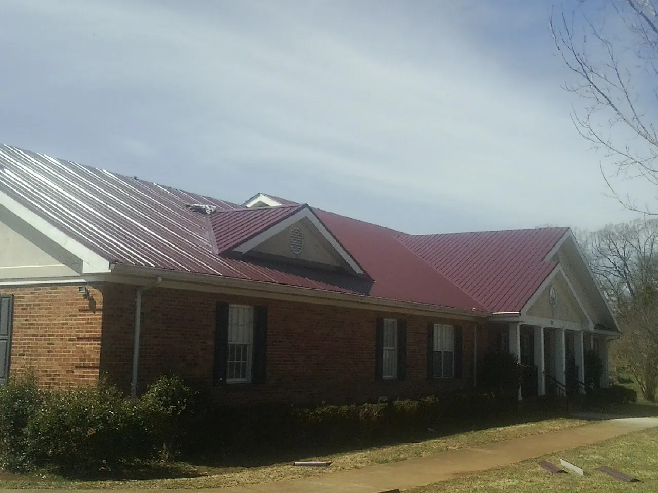 Red metal roof with gabled entries on a long brick building, from a Hail Damage Roof Repair job in Ihlen