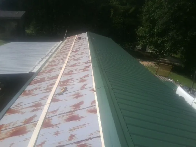 Old rusted panels beside newly installed green metal roofing — Wind Damage Roof Repair by Roofing Brothers in Ihlen