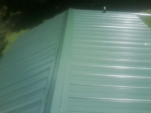 New green metal panels meeting at the ridge of a roof — Flat Roof Repair work by our crew in Ihlen