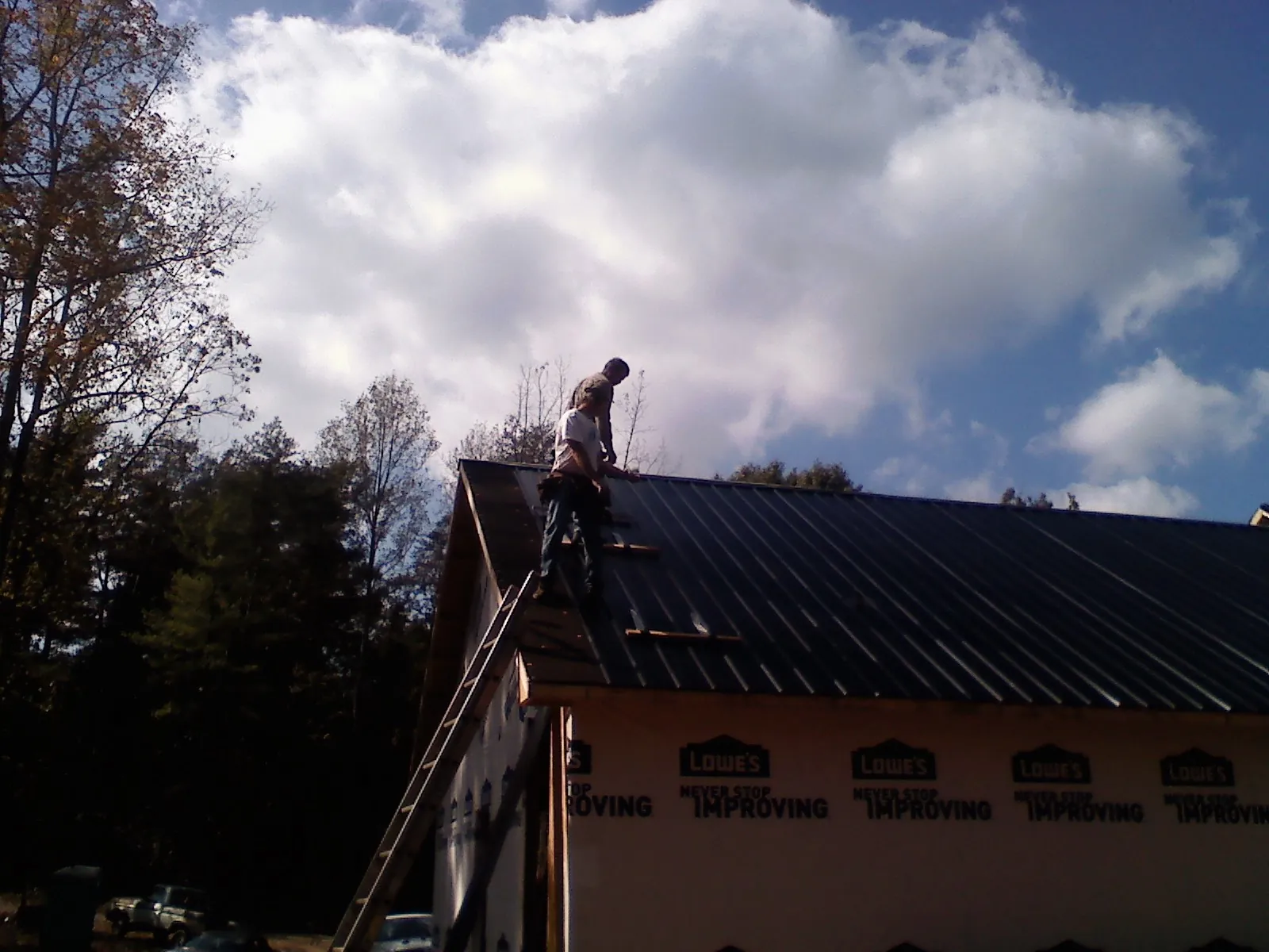 Roofer fastening dark metal panels high against a cloudy sky, from a Roof Inspection job in Ihlen